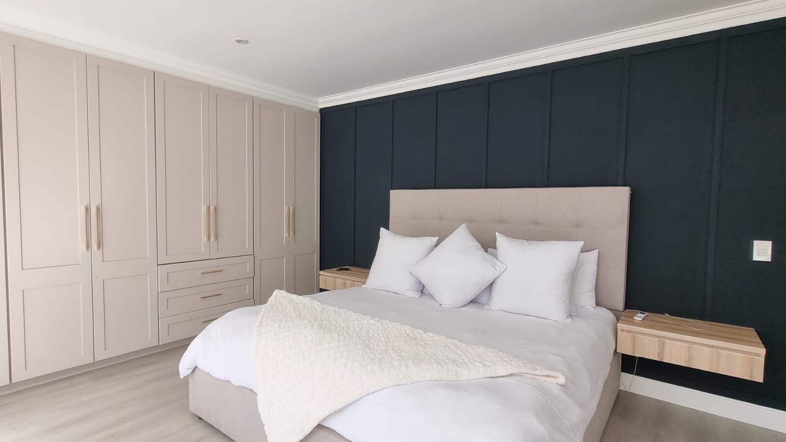 Taupe wardrobe with brass pulls in bedroom with navy panelling